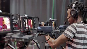 A videographer adjusts camera equipment during a live broadcast in a studio setting.