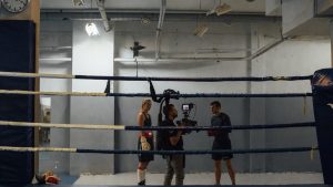 Boxing training scene in an industrial gym with athletes and a videographer capturing the action.