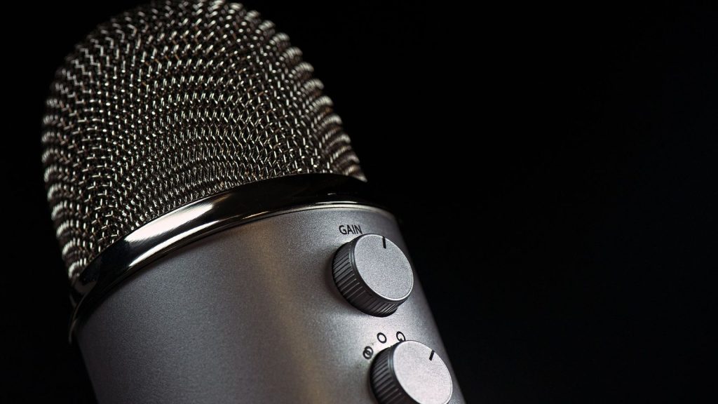 Detailed close-up of a silver mesh microphone with gain control knobs against a dark background.