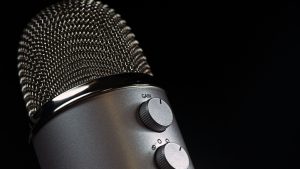 Detailed close-up of a silver mesh microphone with gain control knobs against a dark background.
