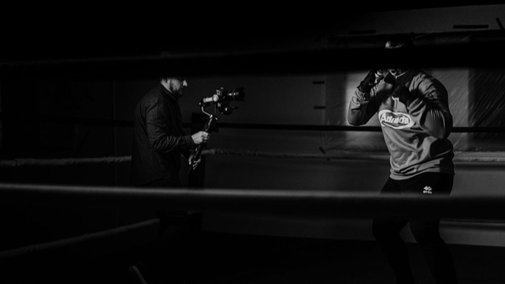 Black and white of crop anonymous sportsman practicing boxing against friend recording video on photo camera for vlog in