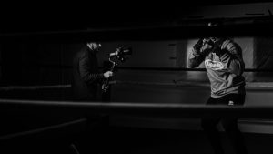 Black and white of crop anonymous sportsman practicing boxing against friend recording video on photo camera for vlog in